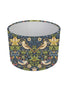 A drum lampshade featuring a classic William Morris-style floral and bird pattern in navy blue, green, yellow, and beige, shown against a plain white background.