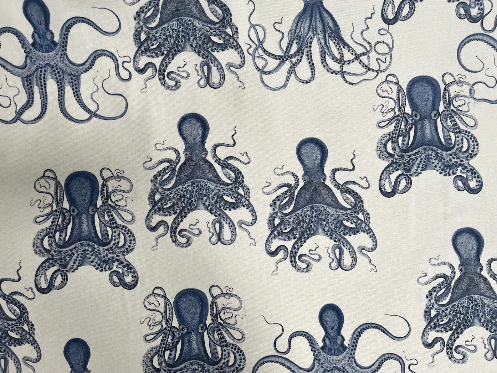 A close-up of a fabric or wallpaper pattern featuring navy blue octopus illustrations on a warm off-white background.
