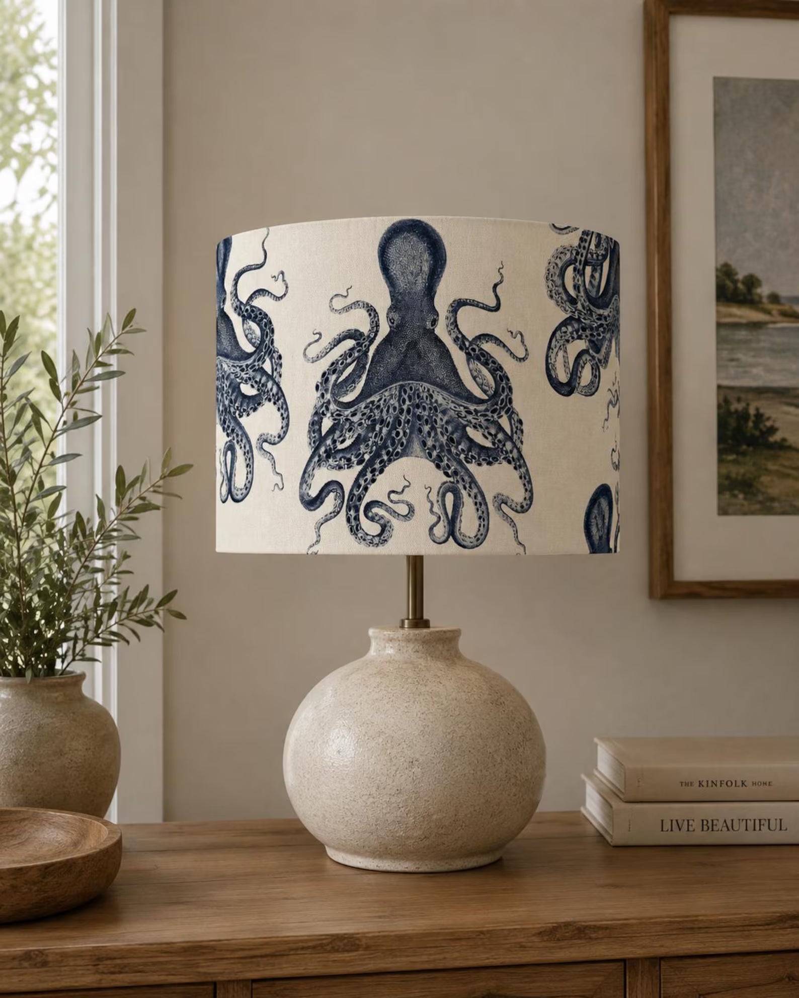 A table lamp with a textured beige ceramic base and a drum shade printed with a navy blue octopus pattern, styled on a wooden console table in a living room setting.