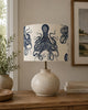 A table lamp with a textured beige ceramic base and a drum shade printed with a navy blue octopus pattern, styled on a wooden console table in a living room setting.